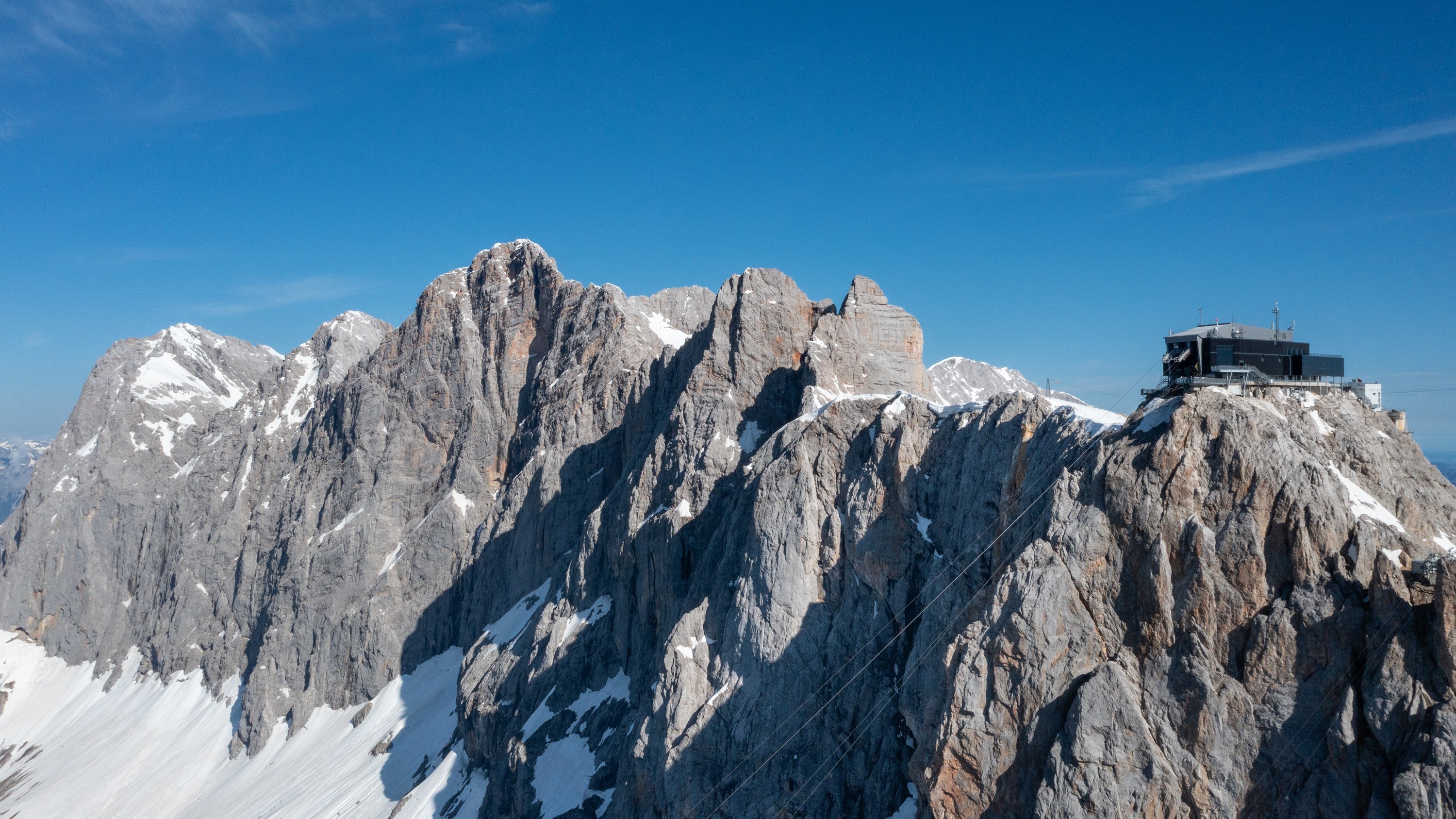 Berglandschaft von oben Luftaufnahme einer gebirgigen Landschaft mit schneebedeckten Gipfeln und einem Gebäude auf einer Anhöhe.